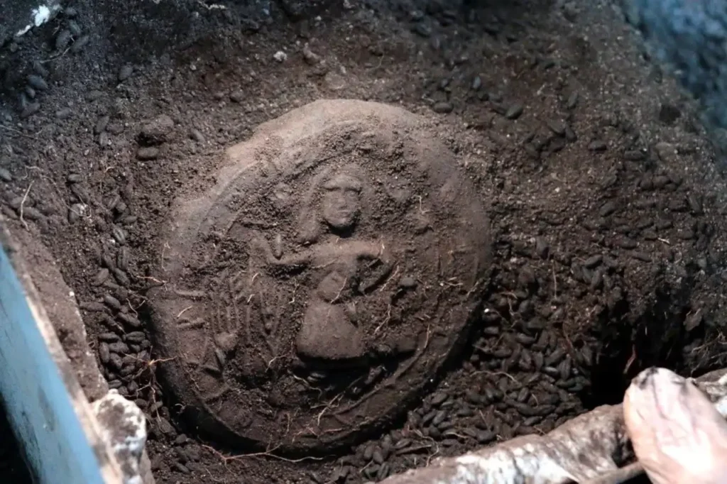 Pan de comunión bizantino de 1300 años parcialmente enterrado, con imagen de Jesucristo en relieve visible sobre la superficie. Hallado entre restos arqueológicos. Autor: desconocido.